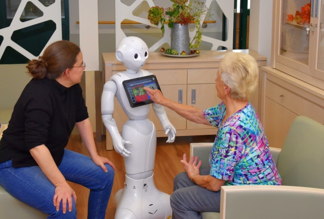 Bewohnerin bedient den humanoiden Roboter Pepper des St. Bonifacius Wohn- und Pflegeheim Unna vor einer Pflegerin